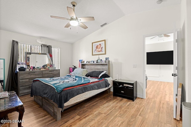 bedroom with ceiling fan, lofted ceiling, light hardwood / wood-style floors, and a textured ceiling