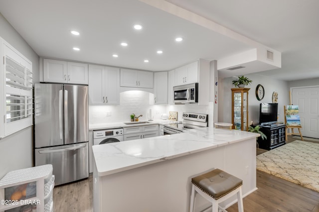 kitchen featuring recessed lighting, light stone counters, a sink, appliances with stainless steel finishes, and washer / clothes dryer