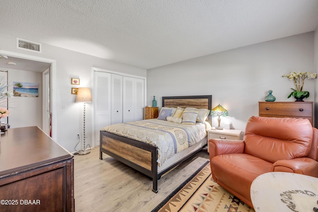 bedroom featuring a closet, light wood-type flooring, visible vents, and a textured ceiling