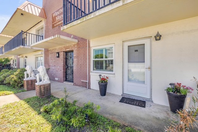 entrance to property featuring brick siding, a balcony, and stucco siding