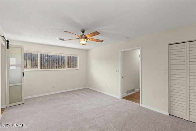 unfurnished bedroom featuring a textured ceiling, a barn door, ceiling fan, and light carpet