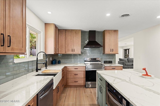 kitchen featuring sink, appliances with stainless steel finishes, light stone countertops, light hardwood / wood-style flooring, and wall chimney range hood