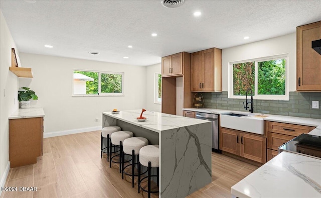 kitchen with light stone counters, a kitchen island, sink, light hardwood / wood-style floors, and stainless steel dishwasher