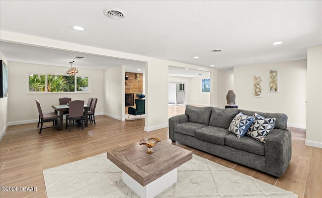 living room with a textured ceiling, a large fireplace, and light hardwood / wood-style flooring