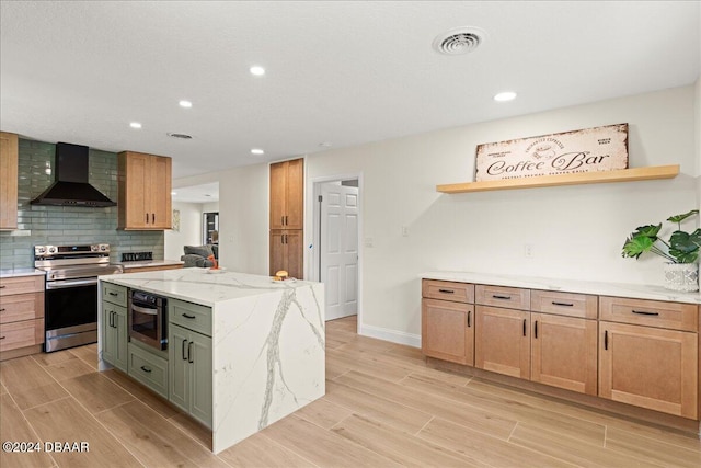 kitchen featuring green cabinetry, stainless steel appliances, wall chimney range hood, a kitchen island, and light hardwood / wood-style flooring