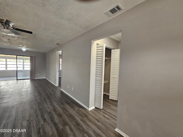 unfurnished room with a textured ceiling, dark wood-style floors, baseboards, visible vents, and ceiling fan