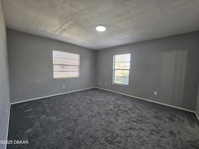 spare room featuring baseboards, dark colored carpet, and a textured ceiling