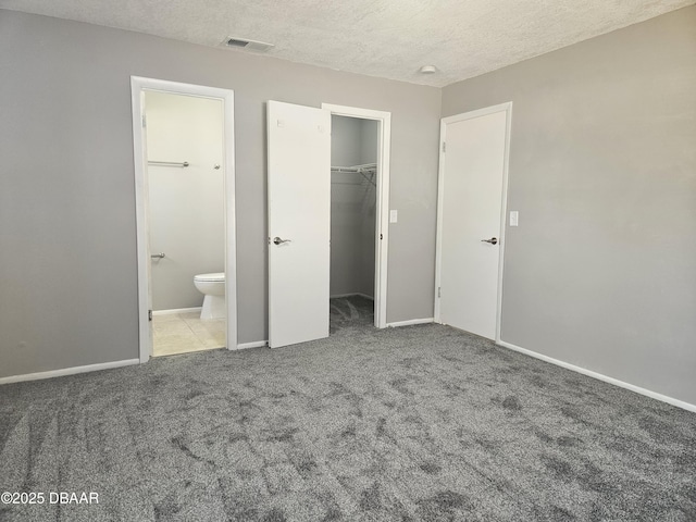 unfurnished bedroom featuring a spacious closet, carpet, baseboards, a textured ceiling, and visible vents