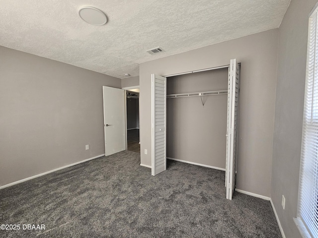 unfurnished bedroom with baseboards, a textured ceiling, dark carpet, visible vents, and a closet