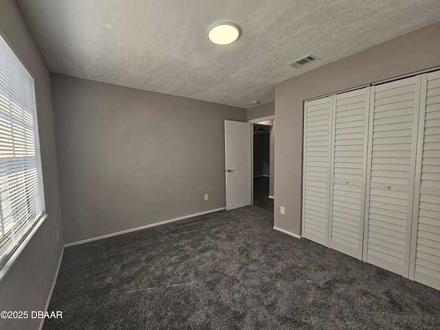 unfurnished bedroom with a closet, a textured ceiling, visible vents, baseboards, and dark colored carpet