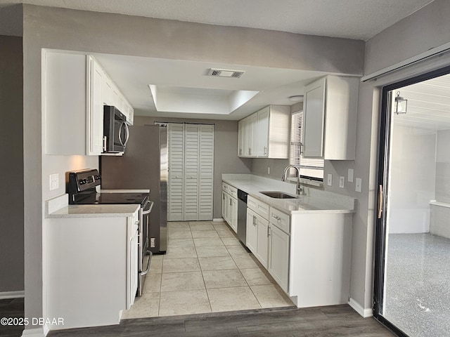 kitchen featuring a tray ceiling, a sink, stainless steel appliances, visible vents, and white cabinets