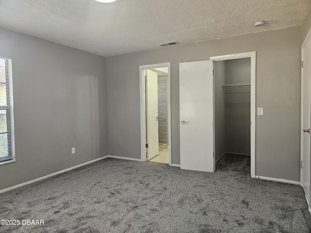 unfurnished bedroom featuring a textured ceiling, visible vents, carpet, baseboards, and a spacious closet