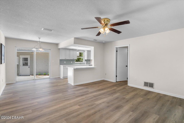 unfurnished living room with ceiling fan with notable chandelier and wood-type flooring