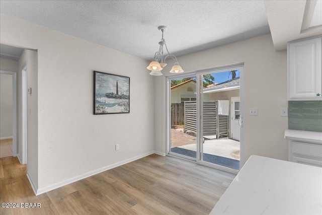 unfurnished dining area featuring an inviting chandelier, a textured ceiling, and light hardwood / wood-style flooring