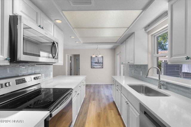 kitchen with appliances with stainless steel finishes, pendant lighting, sink, white cabinetry, and backsplash