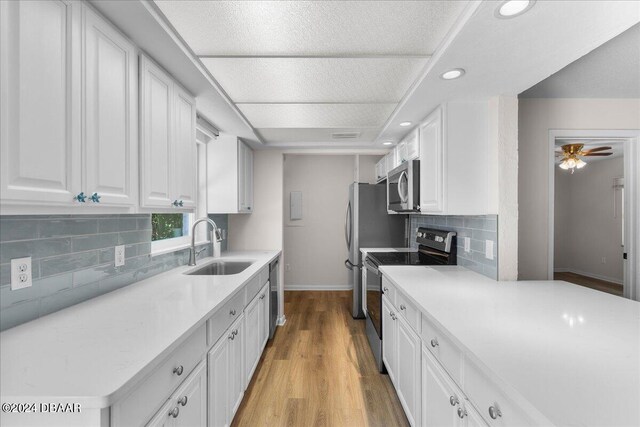 kitchen featuring stainless steel appliances, ceiling fan, decorative backsplash, white cabinets, and sink