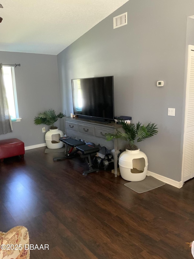 living room featuring lofted ceiling, visible vents, baseboards, and wood finished floors