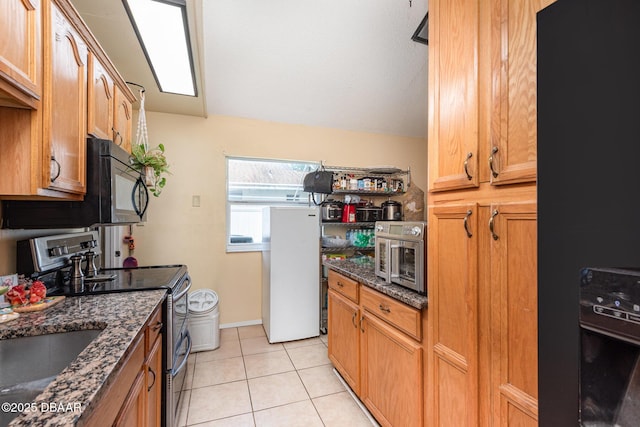 kitchen with black microwave, freestanding refrigerator, dark stone countertops, and stainless steel electric stove