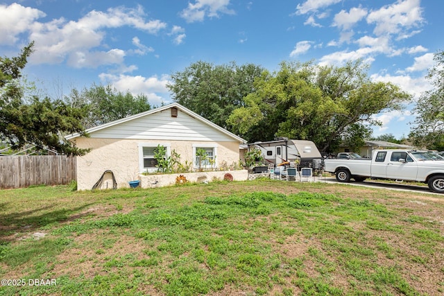 view of front of house with stucco siding, a front lawn, and fence