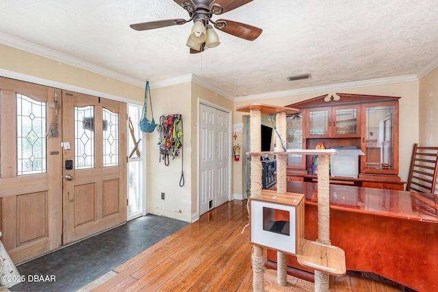 entrance foyer with wood-type flooring, a textured ceiling, a ceiling fan, baseboards, and ornamental molding