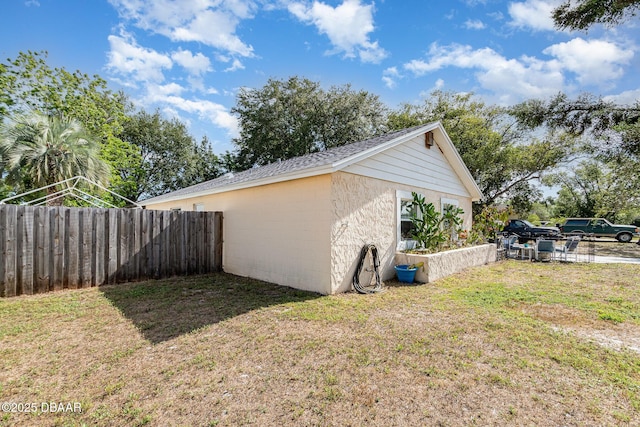 view of home's exterior with a lawn, a shingled roof, concrete block siding, and fence