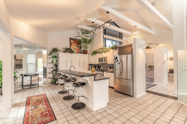 kitchen with dark countertops, a breakfast bar, light tile patterned floors, appliances with stainless steel finishes, and high vaulted ceiling