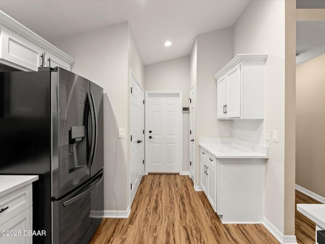 kitchen with light wood-type flooring, stainless steel fridge with ice dispenser, light stone counters, and white cabinets