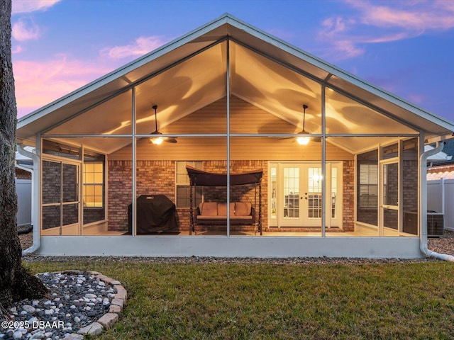 back house at dusk with a lawn, french doors, and central air condition unit