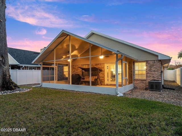 back house at dusk with a yard, a sunroom, and central air condition unit