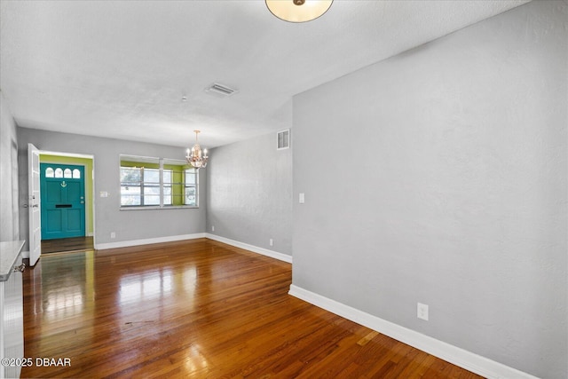 spare room featuring dark wood-type flooring and a notable chandelier