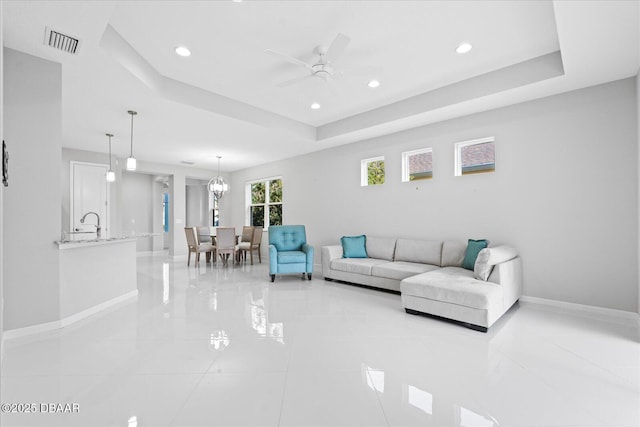 living room with sink, a tray ceiling, and ceiling fan with notable chandelier