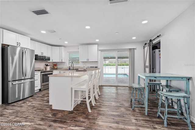 kitchen with a breakfast bar, white cabinets, dark hardwood / wood-style floors, a barn door, and stainless steel appliances