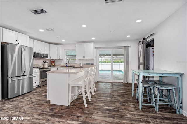 kitchen featuring white cabinets, a barn door, stainless steel appliances, and dark hardwood / wood-style floors