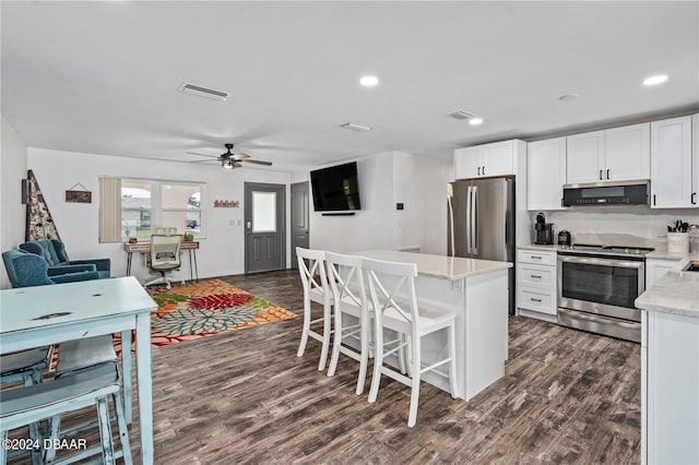 kitchen featuring ceiling fan, stainless steel appliances, dark hardwood / wood-style floors, a kitchen bar, and white cabinets