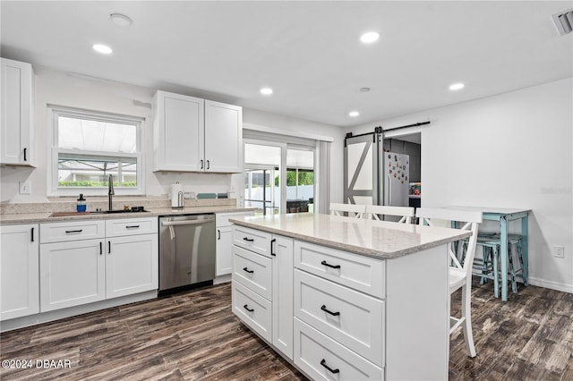 kitchen with dishwasher, dark hardwood / wood-style floors, a barn door, a kitchen bar, and white cabinetry