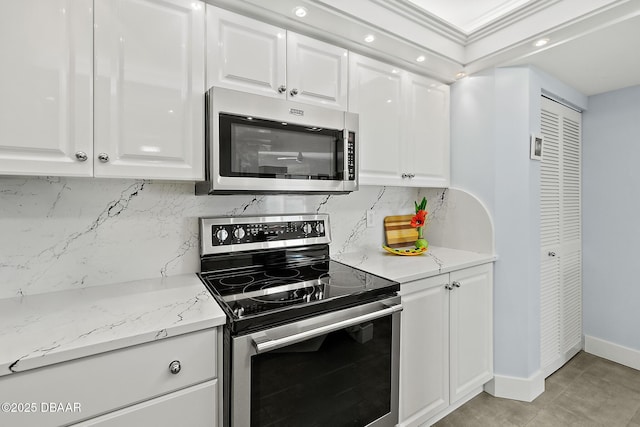 kitchen featuring white cabinetry, crown molding, light tile patterned floors, appliances with stainless steel finishes, and decorative backsplash