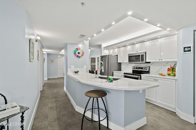 kitchen with tasteful backsplash, a breakfast bar area, white cabinets, stainless steel appliances, and light stone countertops