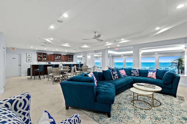 living room with light tile patterned floors, a tray ceiling, ceiling fan, and a water view