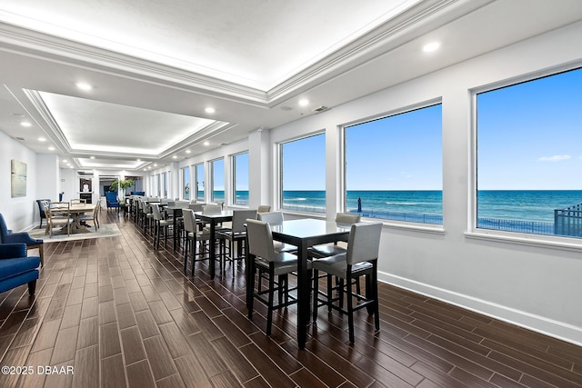 dining area with a water view, ornamental molding, a raised ceiling, and a beach view