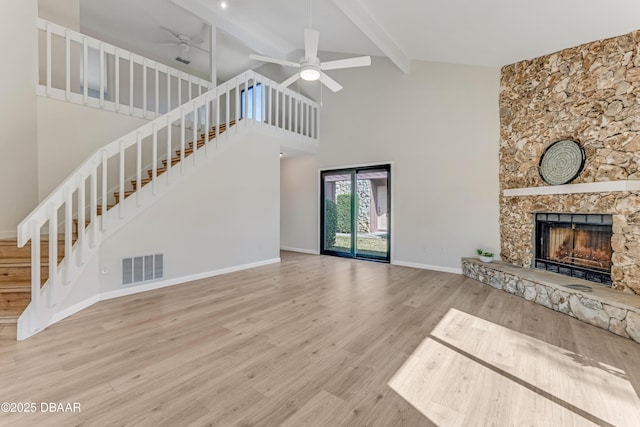 unfurnished living room with ceiling fan, hardwood / wood-style floors, high vaulted ceiling, a stone fireplace, and beamed ceiling