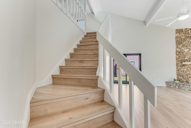 stairway with beamed ceiling, ceiling fan, wood-type flooring, and a high ceiling