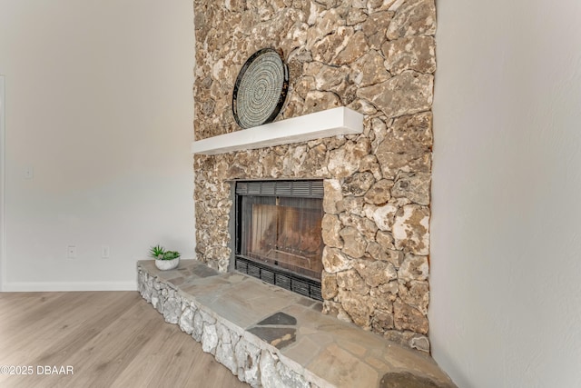 room details featuring baseboards, a fireplace with raised hearth, and wood finished floors