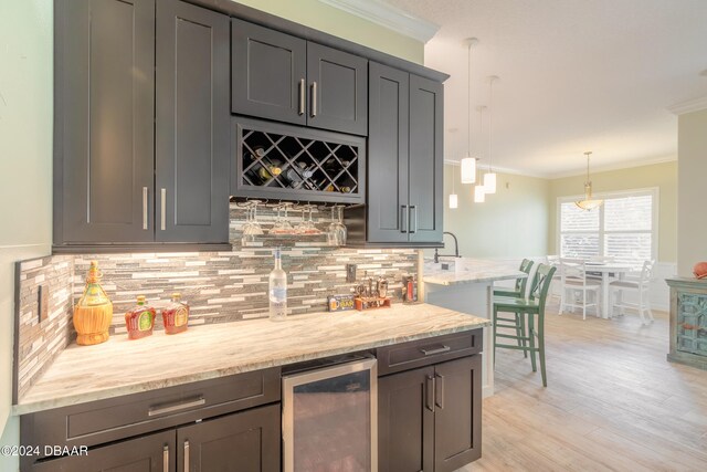 kitchen with crown molding, wine cooler, pendant lighting, light stone countertops, and light hardwood / wood-style floors