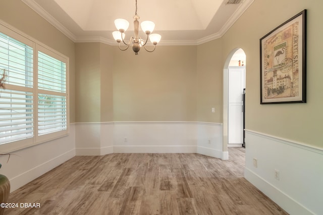 spare room featuring light wood-type flooring, a chandelier, ornamental molding, and a raised ceiling