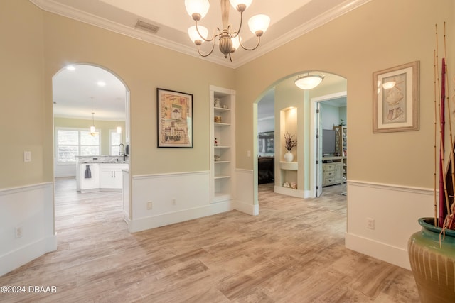 interior space featuring light hardwood / wood-style floors, an inviting chandelier, built in shelves, and ornamental molding