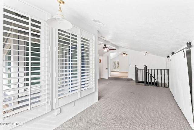 hall featuring carpet flooring, a textured ceiling, a barn door, and vaulted ceiling