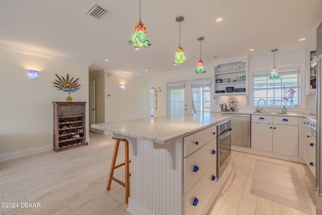 kitchen featuring pendant lighting, a center island, stainless steel oven, white cabinets, and ornamental molding