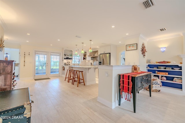 kitchen with hanging light fixtures, light wood-type flooring, high end fridge, a kitchen bar, and white cabinetry