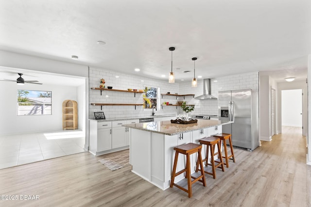 kitchen with white cabinetry, wall chimney range hood, decorative backsplash, a kitchen island, and appliances with stainless steel finishes