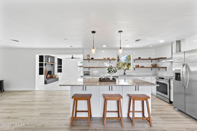 kitchen featuring appliances with stainless steel finishes, backsplash, a center island, and wall chimney range hood